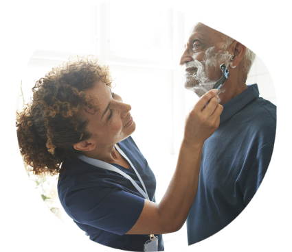 Une aide à domicile rase la barbe d'un bénéficiaire âgé.